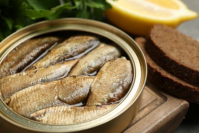 Photo of Tin can with tasty sprats served on wooden board, closeup