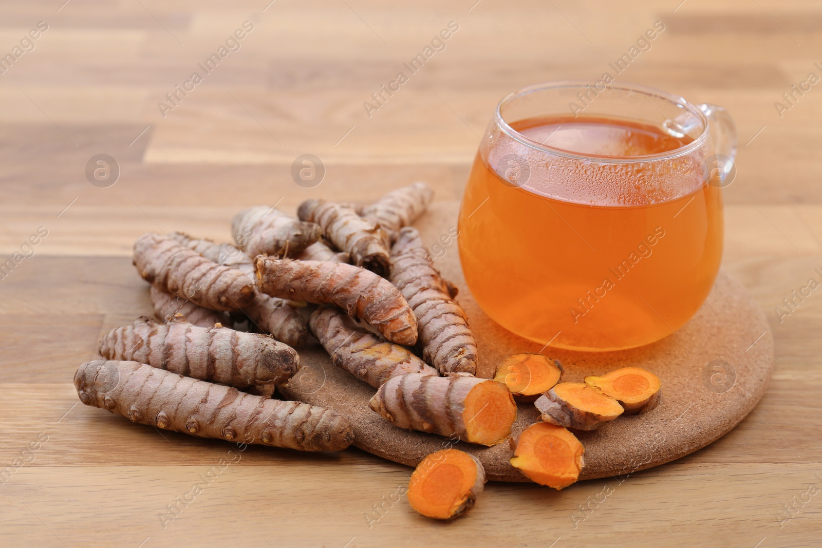 Photo of Glass cup of hot tea and fresh turmeric roots on wooden table