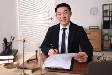 Photo of Happy notary writing notes at wooden table in office