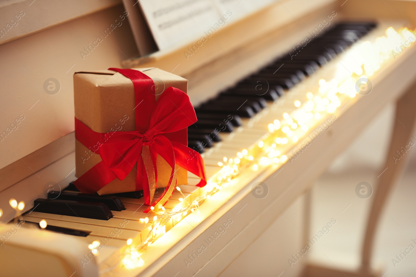 Photo of Gift box and fairy lights on piano keys, space for text. Christmas music