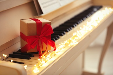 Photo of Gift box and fairy lights on piano keys, space for text. Christmas music