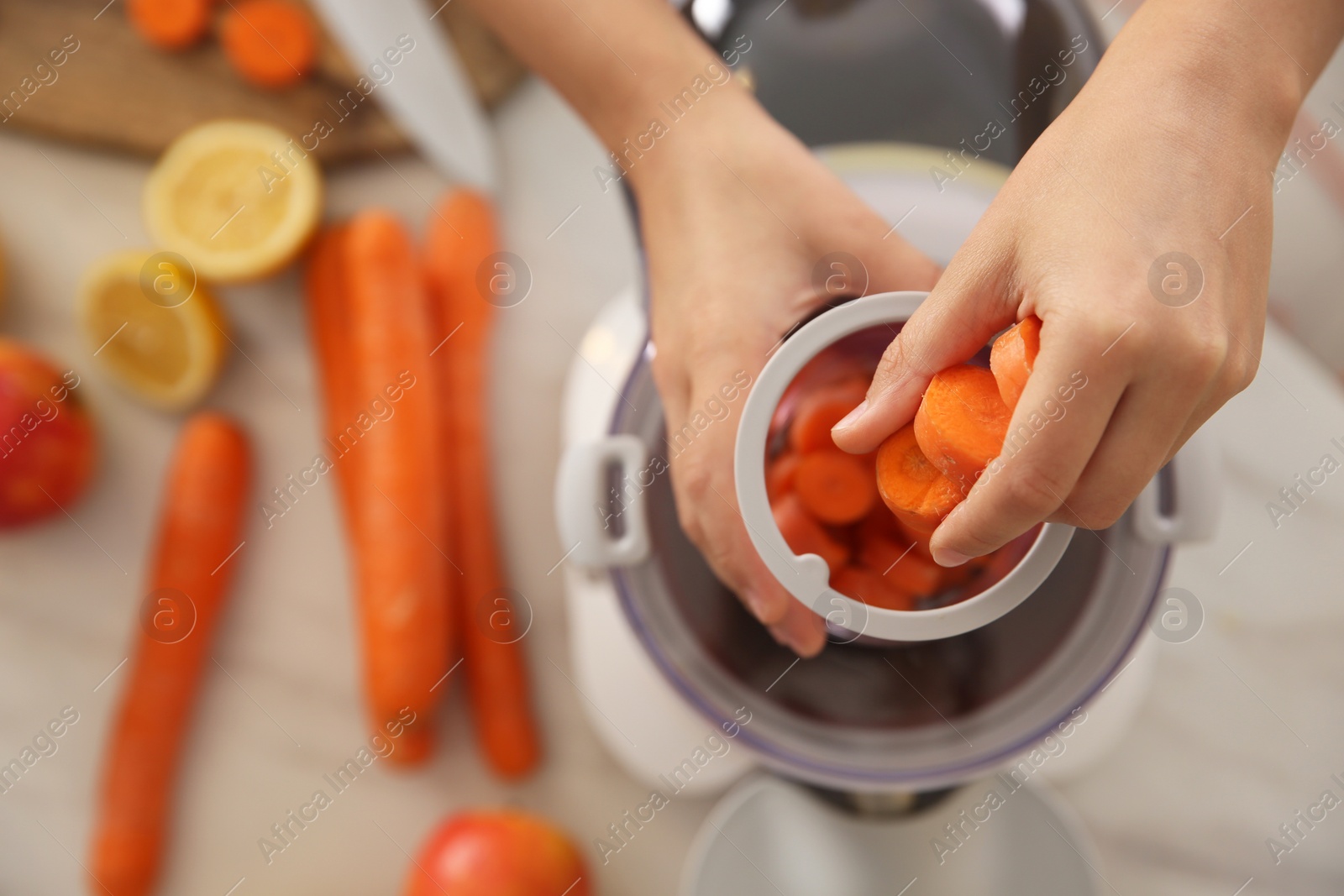 Photo of Young woman putting fresh slices of carrot into juicer at table, top view