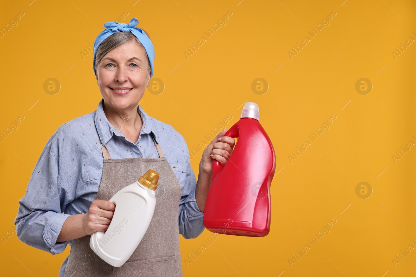 Photo of Happy housewife with bottles of detergent on orange background, space for text