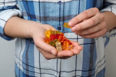 Woman holding colorful jelly bears on light background, closeup