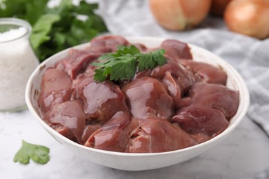 Photo of Bowl of raw chicken liver with parsley on white table, closeup