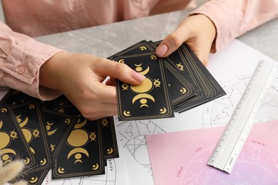 Woman using tarot cards at table, closeup. Astrological predictions