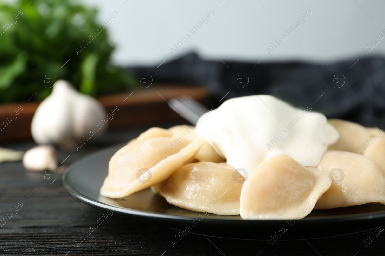 Photo of Delicious cooked dumplings with sour cream on dark wooden table, closeup