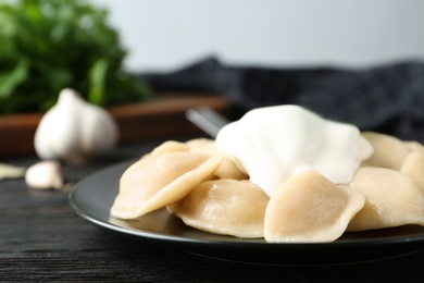 Photo of Delicious cooked dumplings with sour cream on dark wooden table, closeup