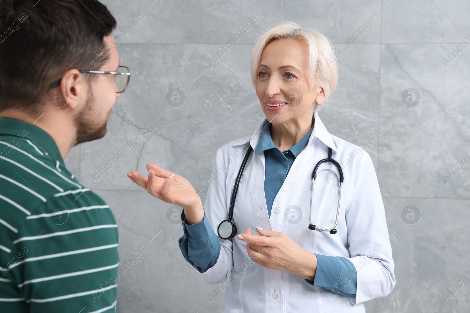 Photo of Happy doctor and patient talking during consultation near grey wall