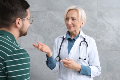 Photo of Happy doctor and patient talking during consultation near grey wall