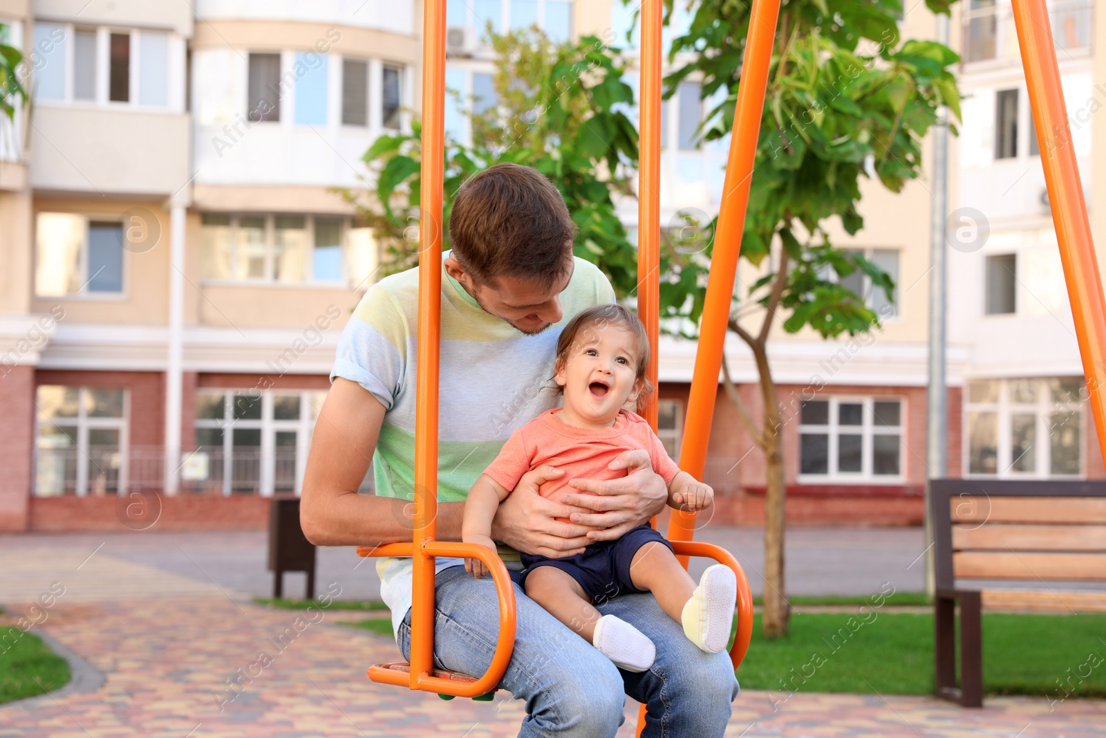 Photo of Father with adorable little baby on swing outdoors. Happy family