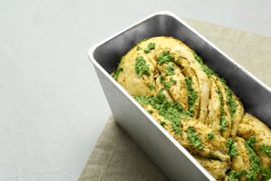 Uncooked pesto bread in baking dish on light table, space for text