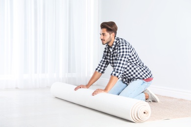 Photo of Man rolling out new carpet flooring indoors. Space for text