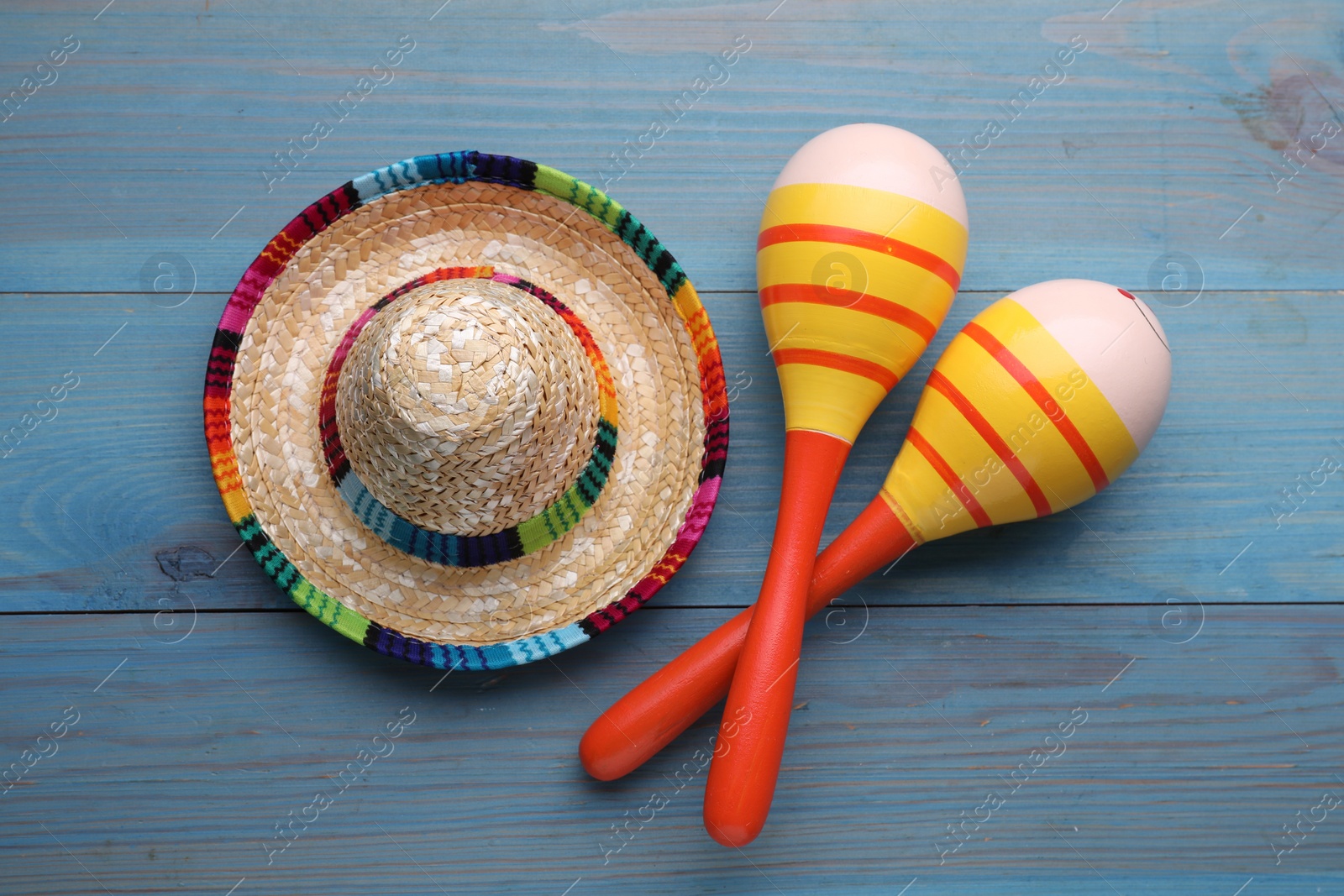 Photo of Colorful maracas and sombrero hat on light blue wooden table, flat lay. Musical instrument