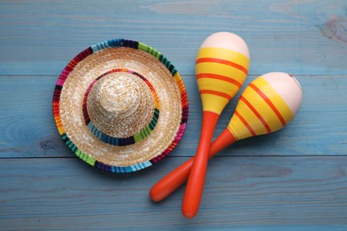 Photo of Colorful maracas and sombrero hat on light blue wooden table, flat lay. Musical instrument