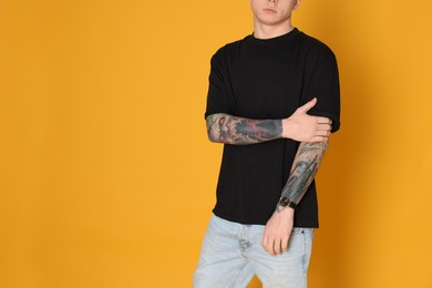Photo of Man with stylish tattoos on yellow background, closeup. Space for text