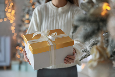 Photo of Woman holding Christmas gift box in festive room interior