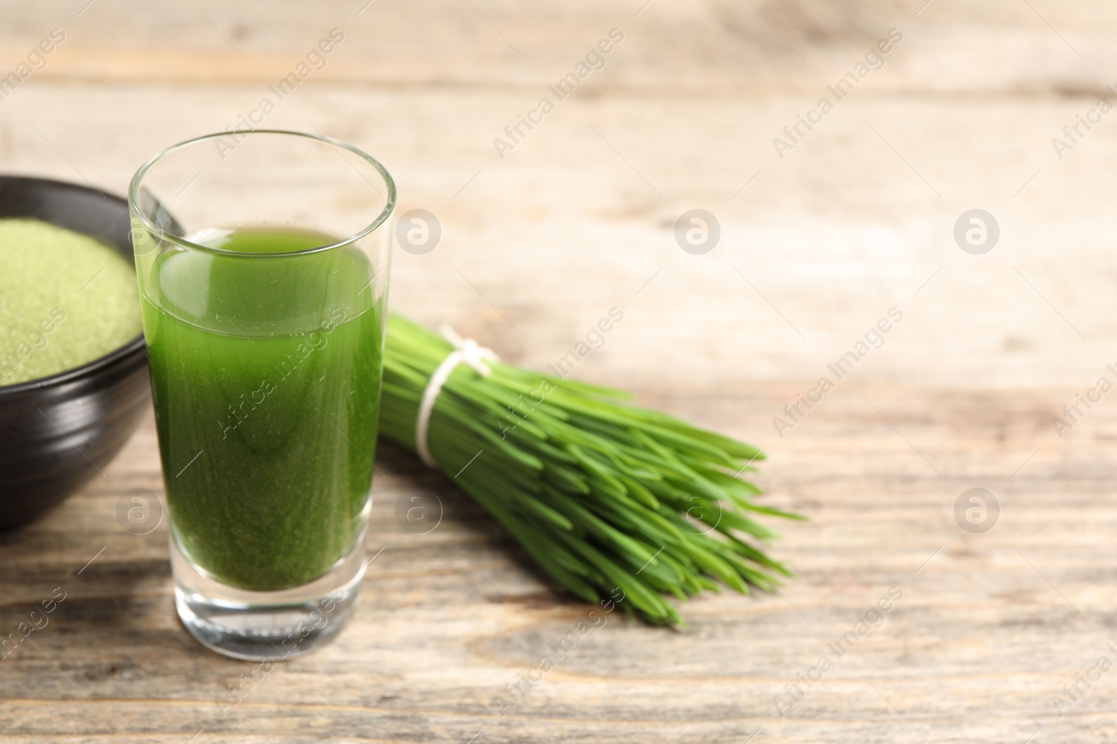 Photo of Wheat grass drink in shot glass and fresh green sprouts on wooden table, closeup. Space for text
