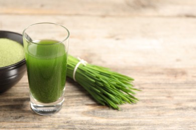 Wheat grass drink in shot glass and fresh green sprouts on wooden table, closeup. Space for text