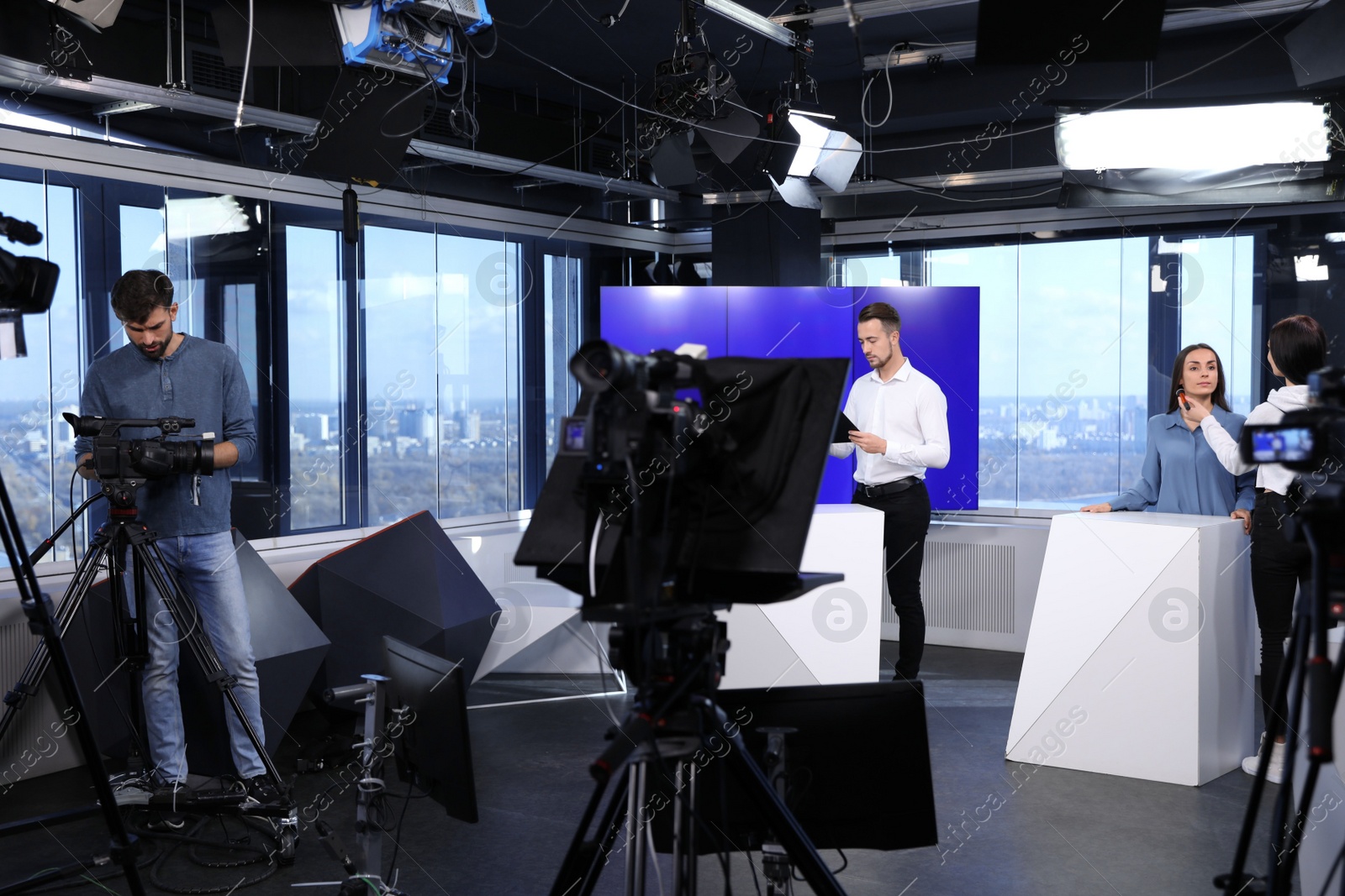 Photo of Presenters, makeup artist and video camera operator working in studio. News broadcasting