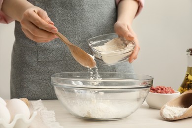 Photo of Woman putting flour into bowl at white wooden table, closeup