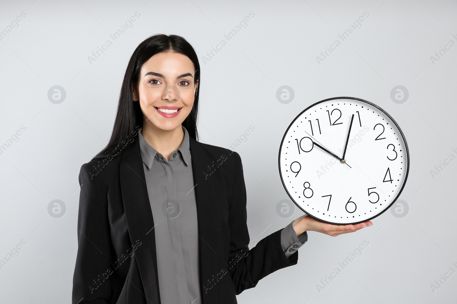 Photo of Businesswoman holding clock on light grey background. Time management