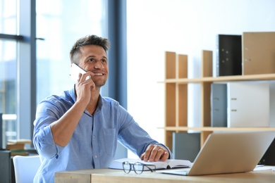 Photo of Male business trainer talking on phone while working with laptop in office