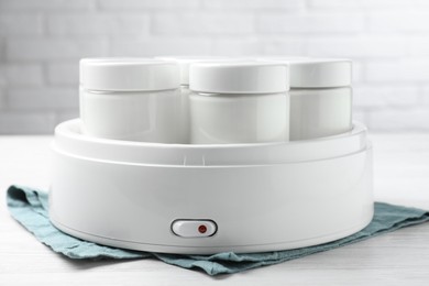 Modern yogurt maker with full jars on white wooden table