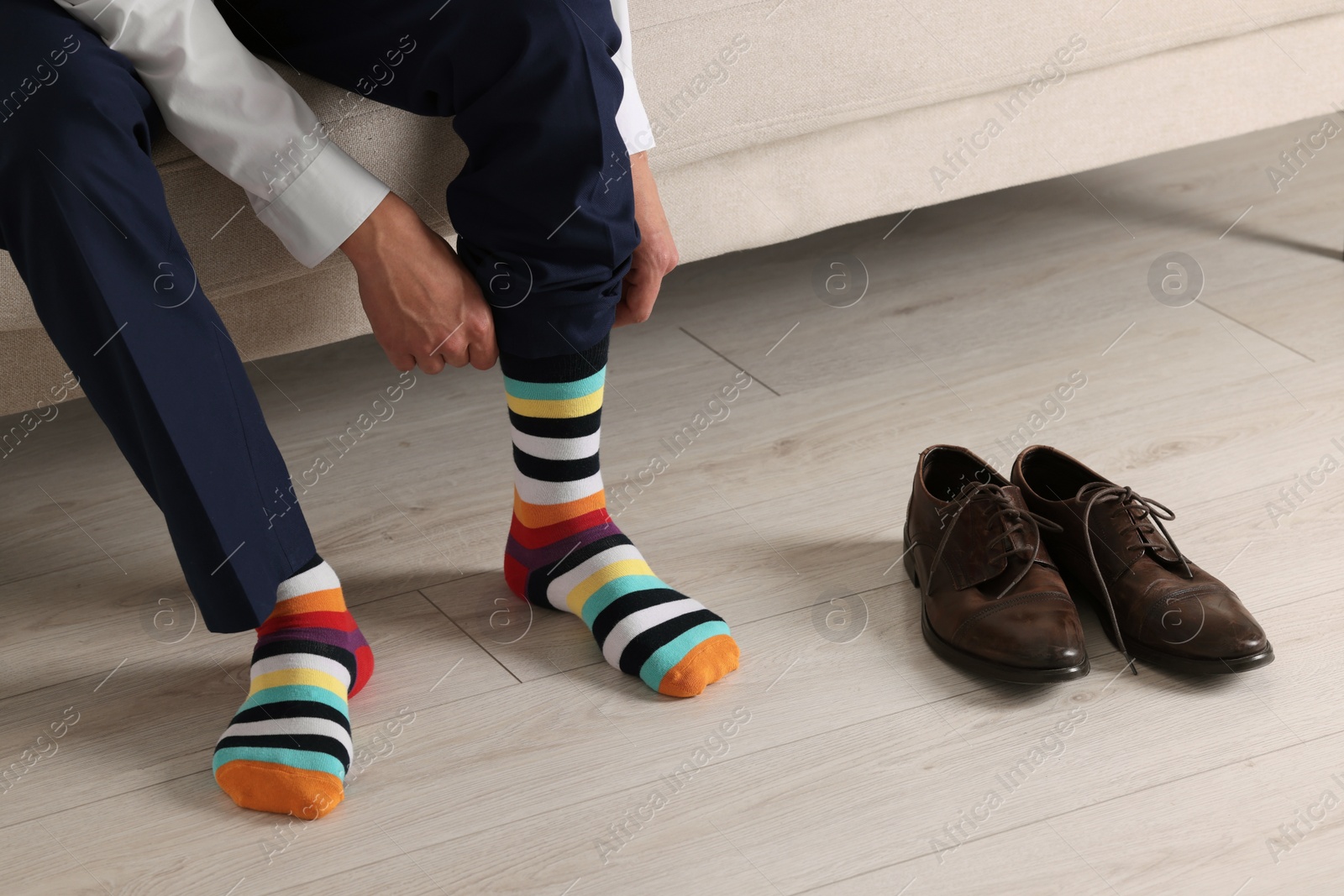 Photo of Man putting on colorful socks indoors, closeup