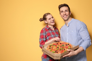 Attractive young couple with delicious pizza on color background