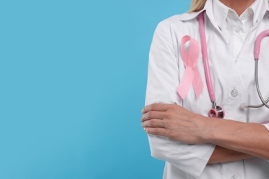 Photo of Doctor with pink ribbon and stethoscope on light blue background, closeup and space for text. Breast cancer awareness