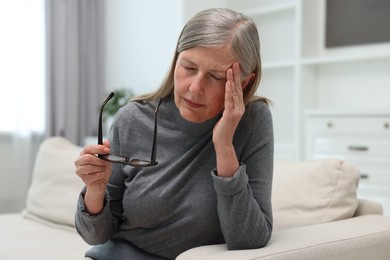 Overwhelmed woman with glasses sitting on sofa at home