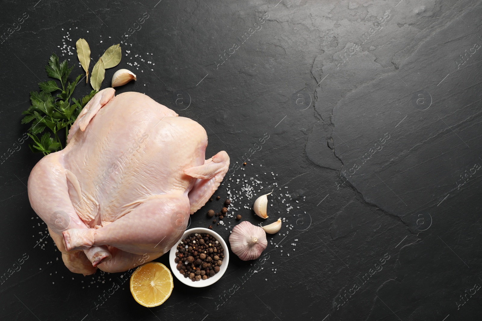 Photo of Fresh raw chicken with spices and lemon on black textured table, flat lay. Space for text