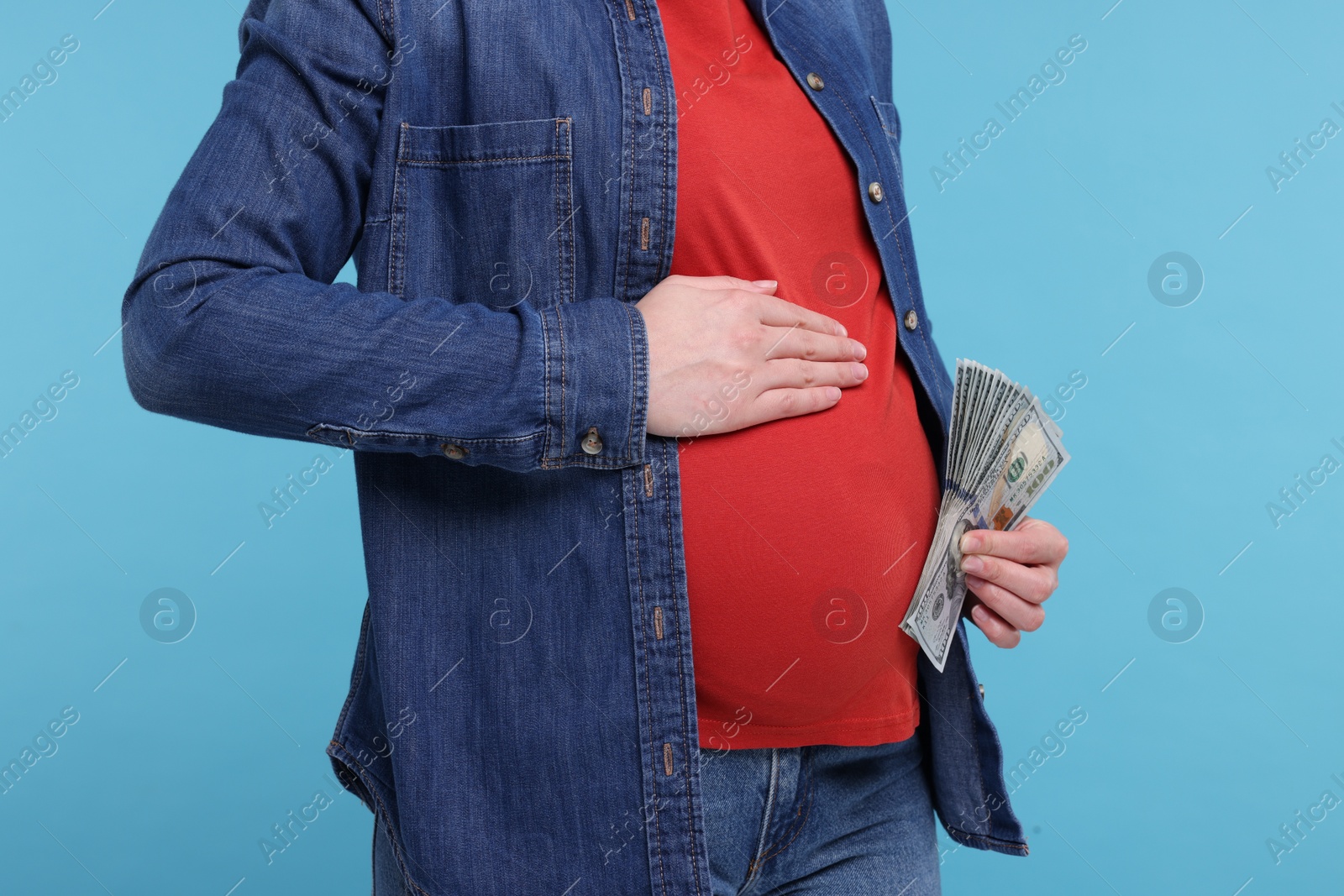 Photo of Surrogate mother. Pregnant woman with dollar banknotes on light blue background, closeup