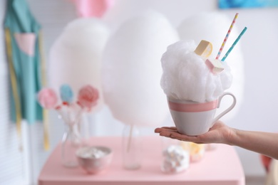 Photo of Woman holding cup with cotton candy dessert on blurred background, closeup. Space for text