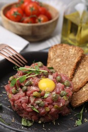 Photo of Tasty beef steak tartare served with yolk, capers and bread in serving pan, closeup