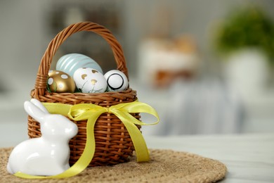 Photo of Small Easter basket with painted eggs near rabbit figure on white marble table. Space for text