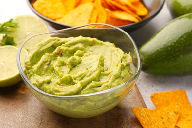 Photo of Bowl of delicious guacamole served with nachos chips and lime on table, closeup
