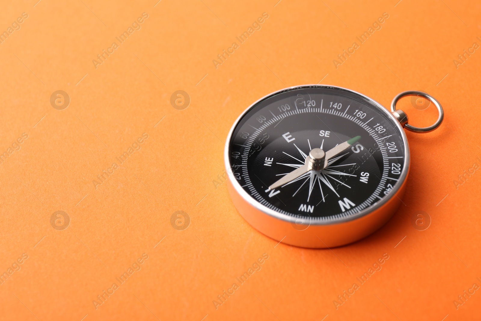 Photo of One compass on orange background, space for text. Tourist equipment