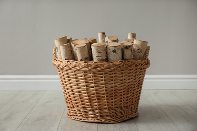 Wicker basket with firewood near grey wall indoors