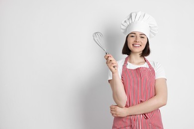 Happy confectioner holding whisk on light grey background, space for text