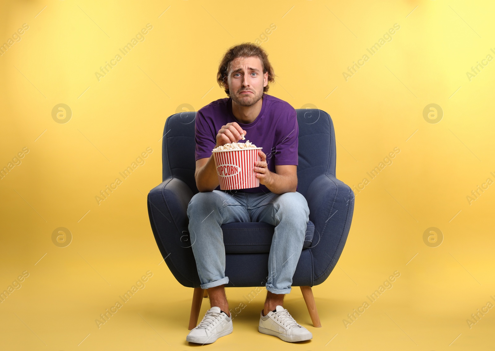 Photo of Emotional man with popcorn sitting in armchair during cinema show on color background