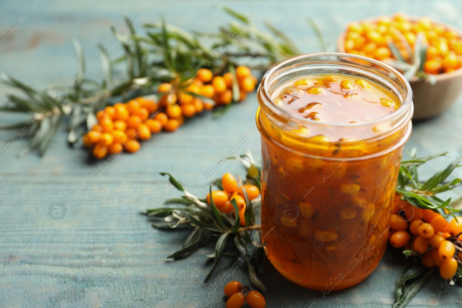 Photo of Delicious sea buckthorn jam and fresh berries on blue wooden table. Space for text