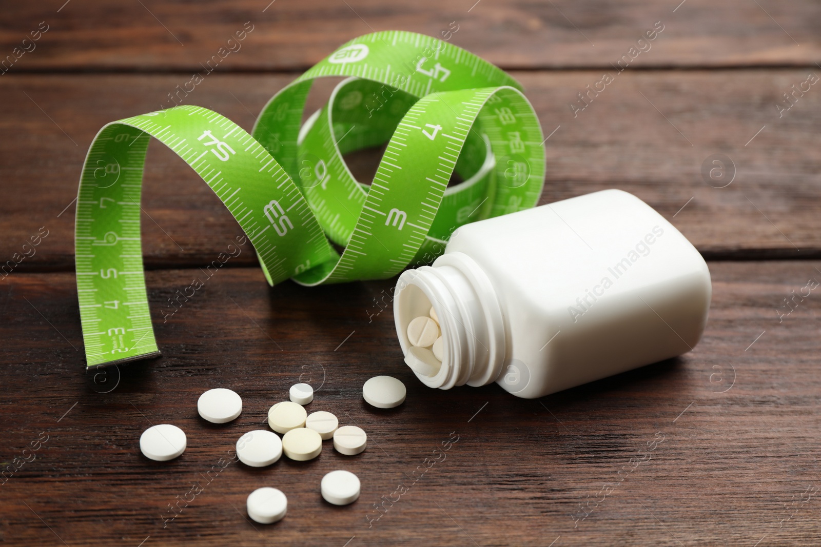 Photo of Jar of weight loss pills and measuring tape on wooden table