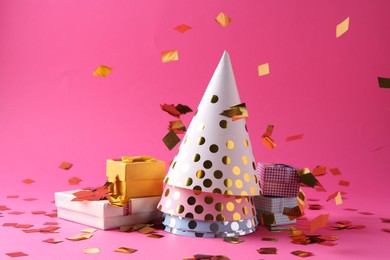 Party hats, gift boxes and confetti on pink background