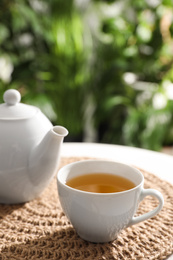 White cup of tea and teapot on table against blurred background