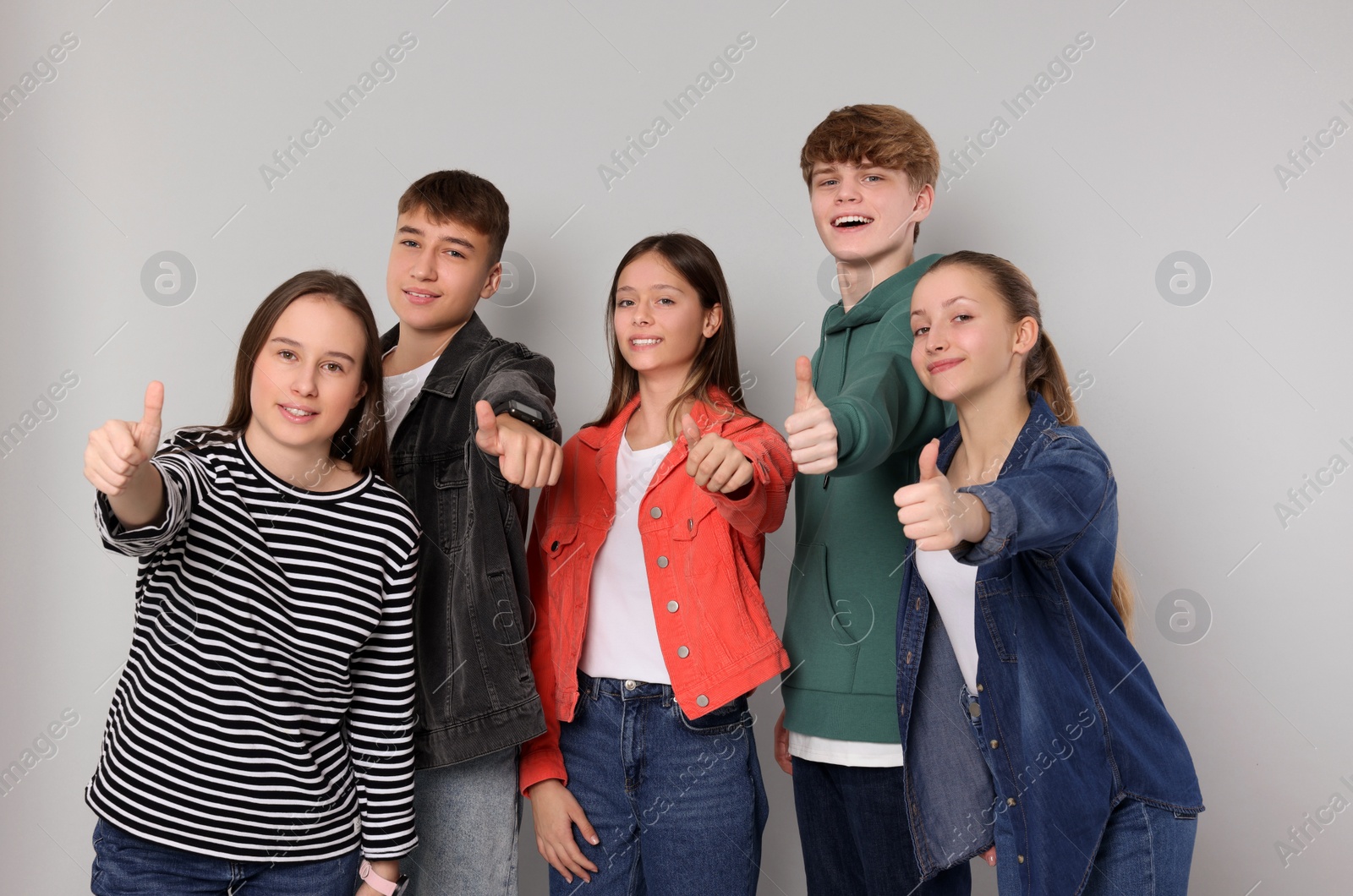 Photo of Group of happy teenagers showing thumbs up on light grey background