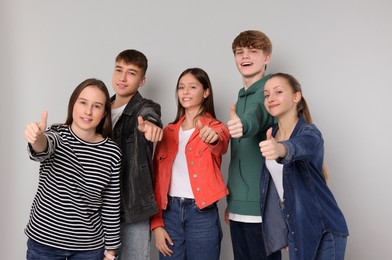 Photo of Group of happy teenagers showing thumbs up on light grey background