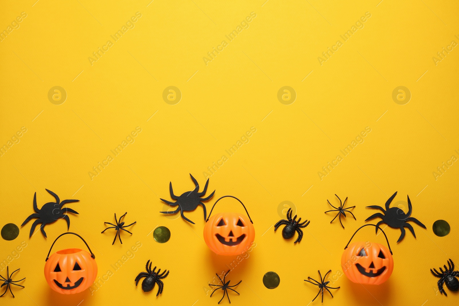 Photo of Flat lay composition with plastic pumpkin baskets, spiders and golden confetti on yellow background, space for text. Halloween celebration
