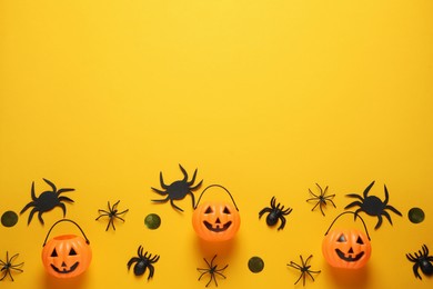 Flat lay composition with plastic pumpkin baskets, spiders and golden confetti on yellow background, space for text. Halloween celebration